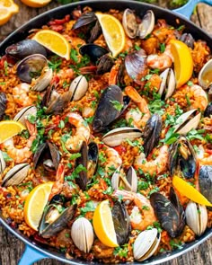 a pan filled with seafood and rice on top of a wooden table next to lemon wedges