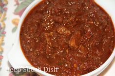 a white bowl filled with chili sauce on top of a floral tablecloth covered table