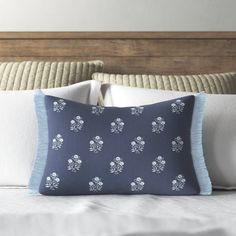 a blue pillow with white flowers on it sitting on top of a bed next to a wooden headboard