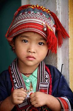 a little boy wearing a colorful hat and holding something in his hand while standing next to a door