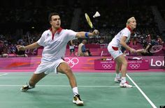 two men playing tennis on a court with people watching from the stands in the background