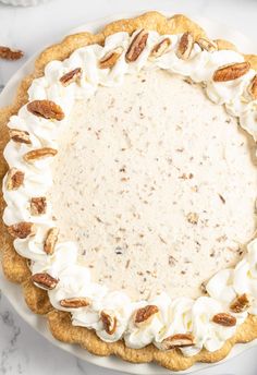 a white plate topped with a pie covered in whipped cream and pecans on top of a marble table