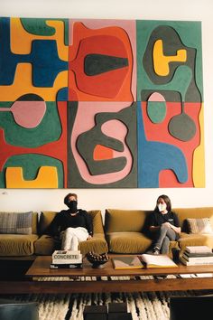 two people sitting on a couch in front of a large abstract painting over a coffee table