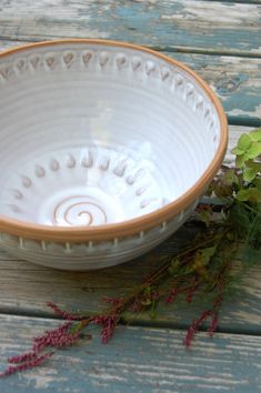 a white and brown bowl sitting on top of a wooden table next to some flowers