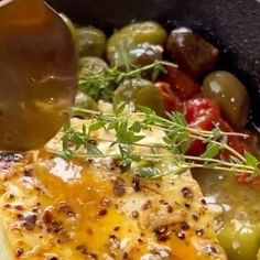 a pan filled with chicken, olives and tomatoes being drizzled over it