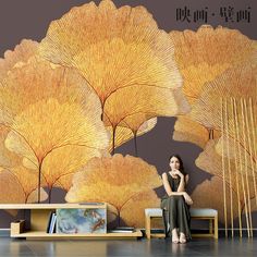 a woman sitting on a bench in front of a wall mural with yellow leaves and bamboo sticks