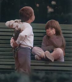 two children are sitting on a bench and one is holding flowers while the other looks at him