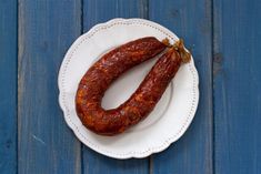 two sausages on a white plate sitting on a blue wooden table top, one is cooked and the other is uncooked