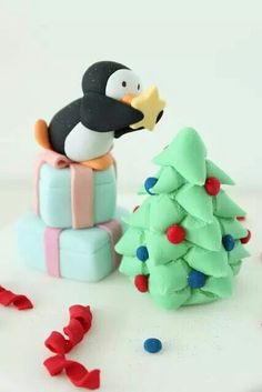 a penguin sitting on top of a stack of presents next to a small christmas tree