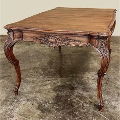 an old wooden table with carvings on the top and legs, sitting on concrete flooring