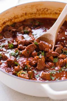 a pot filled with meat and garnish on top of a table next to a wooden spoon