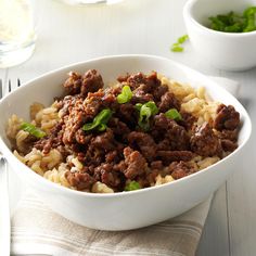 a white bowl filled with meat and rice on top of a table next to silverware