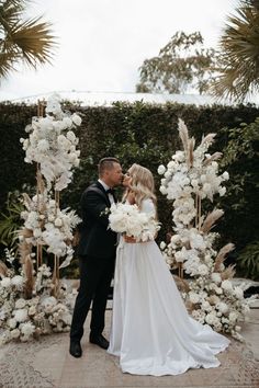 a bride and groom kissing in front of a floral arch