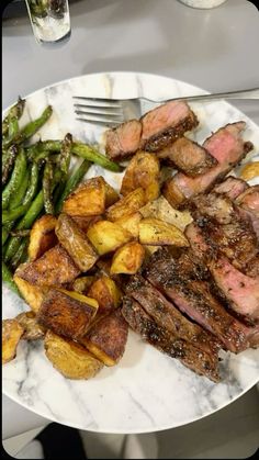 a white plate topped with meat and potatoes next to asparagus on a table