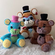 three crocheted teddy bears sitting next to each other on a white blanket with a wall in the background