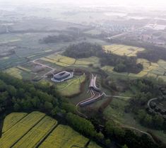 an aerial view of a road surrounded by green fields and trees in the foggy day