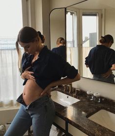 a pregnant woman standing in front of a bathroom mirror