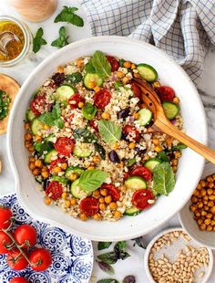 a bowl filled with vegetables and grains next to other foods on a table, including tomatoes, cucumbers, chickpeas