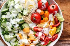 a salad with tomatoes, cucumbers, cheese and lettuce in a white bowl