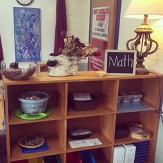 a wooden shelf filled with lots of books and other items next to a lamp on top of a hard wood floor