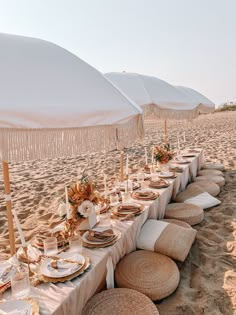 a long table set up on the beach for an outdoor dinner party with white umbrellas