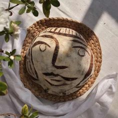 a basket with a face painted on it sitting next to some white flowers and leaves