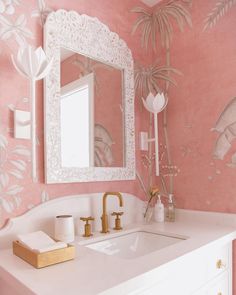 a bathroom with pink and white wallpaper, gold faucet, mirror and sink