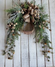 a wreath with pine cones and evergreens hanging on a white wooden wall in front of a door