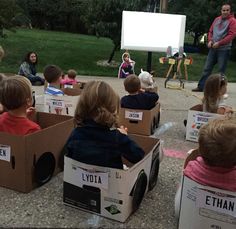 children are sitting in cardboard boxes with signs on them and people standing around the box