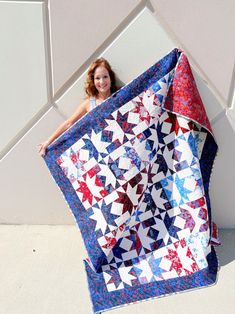 a woman holding up a red, white and blue quilt