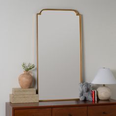 a mirror sitting on top of a wooden dresser next to a lamp and stuffed animal