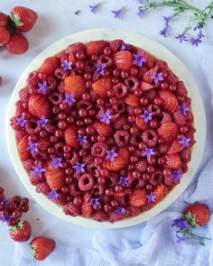 a cake decorated with berries and flowers on a white tablecloth next to strawberries