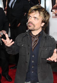 a man with his hands in the air and one hand out, standing on a red carpet