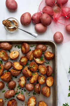 potatoes on a baking sheet with parsley and seasoning in a bowl next to them