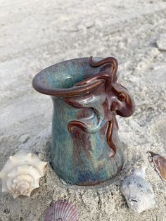 a ceramic vase sitting on top of a sandy beach next to shells and seashells