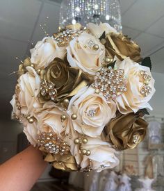 a bridal bouquet is being held by someone's hand in front of a chandelier