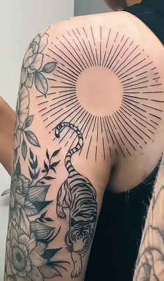 the back of a woman's shoulder with tattoos on her body and sunburst