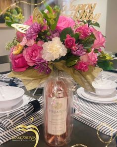 a vase filled with pink flowers sitting on top of a table next to a bottle of wine