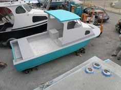 a man standing next to a small boat in a parking lot with other boats behind him