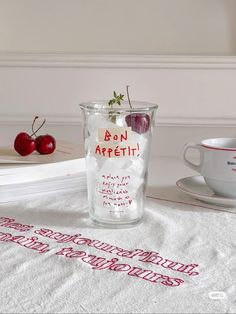 a glass with cherries in it sitting on a table next to a cup and saucer