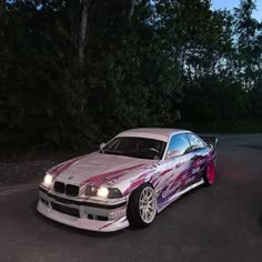 a pink and white car parked on the side of a road next to some trees