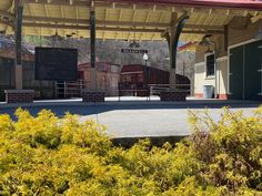 an empty parking lot in front of a train station with trees and bushes around it