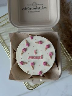 an ice cream cake with pink icing in a white box on a gold tray