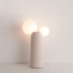 a white vase sitting on top of a table next to a light that is turned on