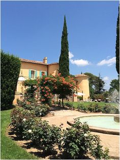 a house with trees and flowers in front of it on a sunny day near a fountain