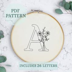 an embroidery pattern with the letter a and flowers on it, surrounded by greenery