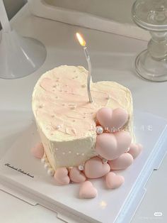 a heart shaped cake with a single candle on it's top surrounded by pink hearts