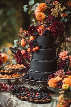 a black wedding cake with berries and flowers on the top is surrounded by other desserts