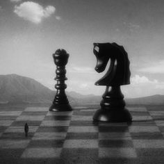 two chess pieces on a checkered board with mountains in the background and a lone figure standing at the end