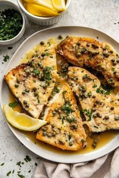 fish with lemon and capers on a white plate next to two bowls of sauce